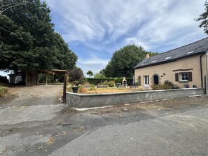 Um imóvel residencial com entrada pavimentada, pérgola de madeira, jardim com diversas plantas e casa com telhado ladrilhado e chaminé.