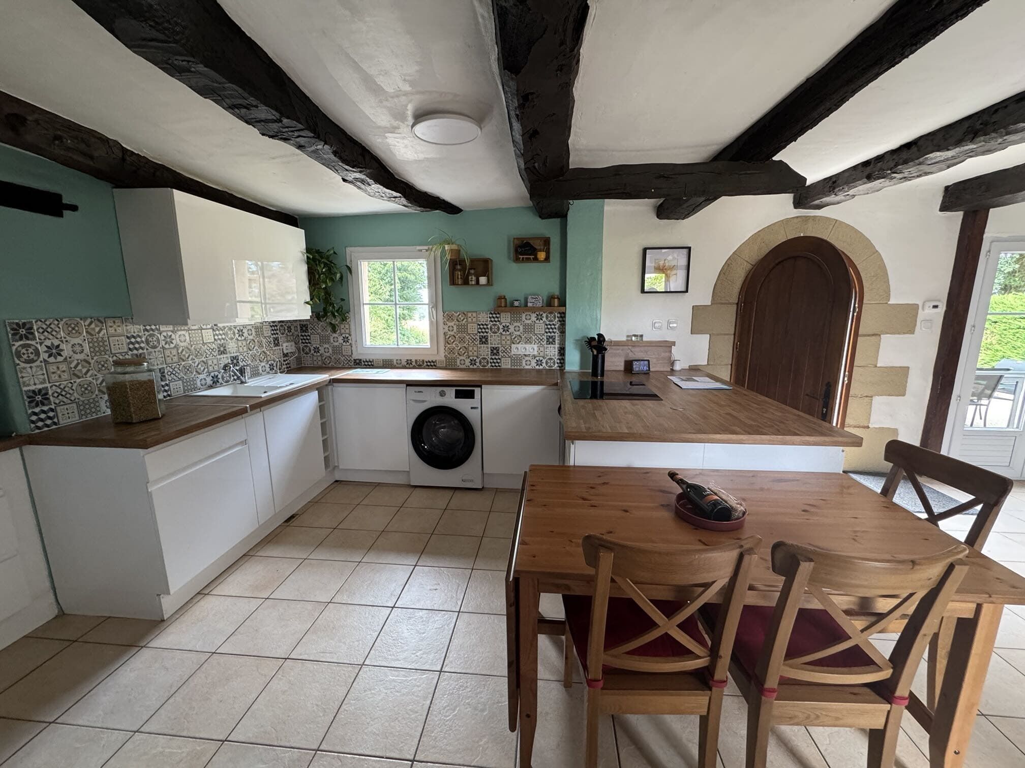 A kitchen with a washing machine, a dining table with chairs, and a wooden door.