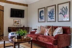 A living room with a red sofa, a coffee table, a flat-screen TV mounted on the wall, and three framed botanical prints. - Violet Cottage -  Brede , Sussex (Brede)