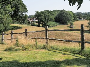 A rural landscape with a wooden fence, grassy fields, and houses in the background. - Violet Cottage -  Brede , Sussex (Brede)