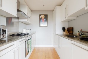 Eine moderne Küche mit weißen Schränken, einer Edelstahl-Dunstabzugshaube, einer Mikrowelle und einem Toaster. Der Boden ist aus Holz und an der Wand hängt ein gerahmtes Kunstwerk.