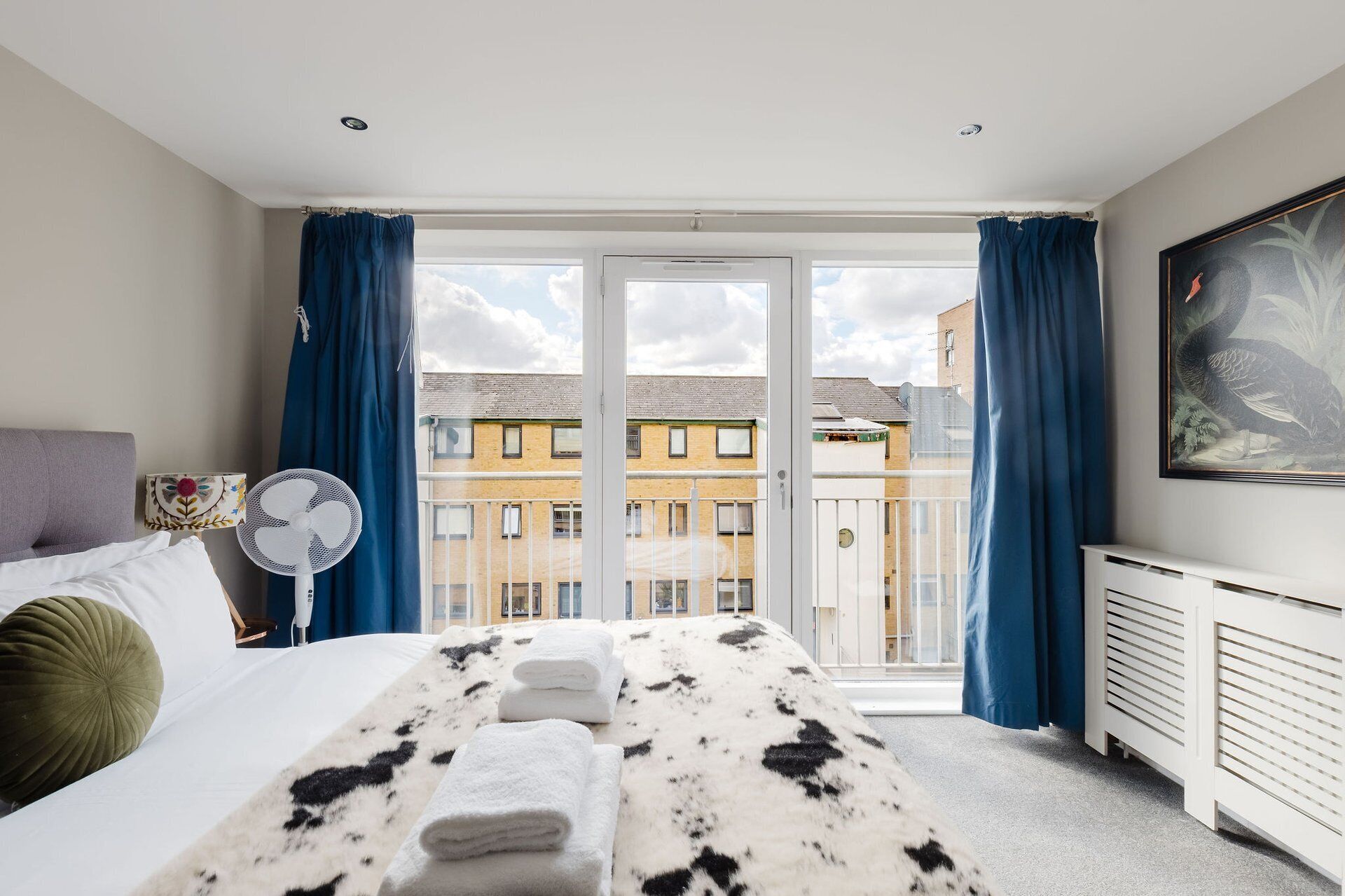 Ein Hotelzimmer mit Bett, Standventilator, Heizkörper und einem großen Fenster mit Vorhängen.