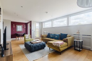 Ein geräumiges Wohnzimmer mit einer Couch, Hocker und einem Essbereich mit Tisch und Stühlen.