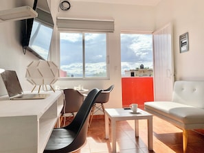 A compact living space with a kitchenette, a dining area with a table and chairs, a sofa, and a large window offering a view of the sky and clouds. - Sky Flat 2_3___600 mbps fibre optic Wifi__ Great mountain views (Oaxaca de Juárez)