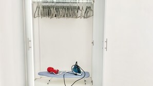 Valkoinen vaatekaappi, jonka ovet ovat auki. Siinä on vaatetanko, tasainen silityslauta ja kaksi laatikkoa.