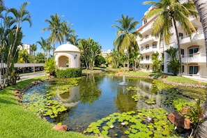 A resort with a pond, palm trees, and a white building with arches. - Costa Bonita Beachfront Family Condo (Mazatlán)