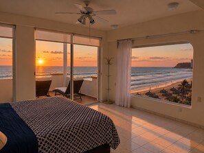 Ein Hotelzimmer mit Bett, einem Balkon mit Blick auf den Strand und den Ozean sowie einem Deckenventilator.