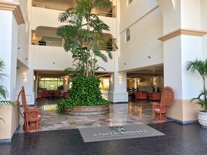 A hotel lobby with a large central plant, multiple seating areas, and a reception desk. - Costa Bonita Beachfront Family Condo (Mazatlán)