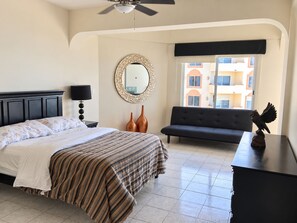 A hotel room with a bed, a sofa, a dresser, a mirror, and a window with a view of buildings. - Costa Bonita Beachfront Family Condo (Mazatlán)