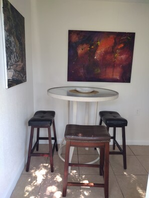 Un coin repas avec une table ronde, deux tabourets et un tableau accroché au mur.