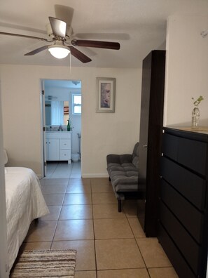 A bedroom with a bed, a gray sofa, a dresser, and a ceiling fan. - Your cozy home near the beach in Hallandale Beach. Close to everything. (Hallandale Beach)