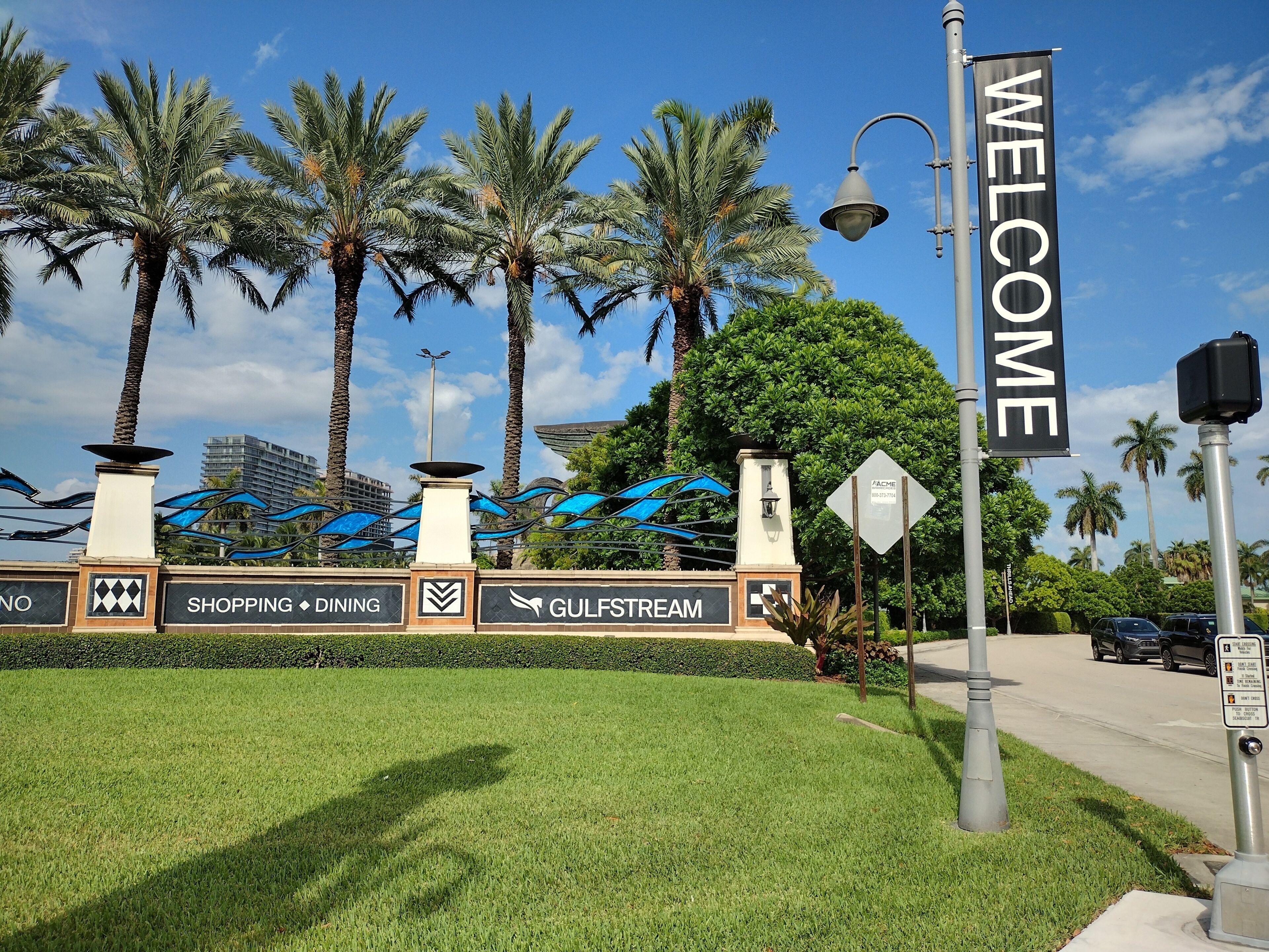 A welcome sign with palm trees and a clear sky.