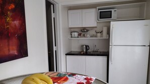 A kitchen with white cabinets, a microwave, a refrigerator, and a table with a banana bowl. - Your cozy home near the beach in Hallandale Beach. Close to everything. (Hallandale Beach)