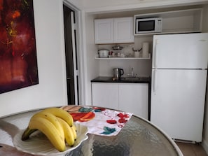 A kitchen with white cabinets, a microwave, a refrigerator, and a table with a banana bowl. - Your cozy home near the beach in Hallandale Beach. Close to everything. (Hallandale Beach)