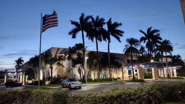 A hotel with a flag, palm trees, and a car parked in front. - Your cozy home near the beach in Hallandale Beach. Close to everything. (Hallandale Beach)