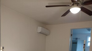 A bedroom with a bed, bedside table, lamp, air conditioning unit, and a ceiling fan. - Your cozy home near the beach in Hallandale Beach. Close to everything. (Hallandale Beach)