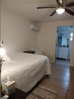 A bedroom with a bed, bedside table, lamp, air conditioning unit, and a ceiling fan. - Your cozy home near the beach in Hallandale Beach. Close to everything. (Hallandale Beach)