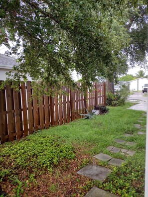 A wooden fence, a grassy area with stepping stones, and a house in the background. - Your cozy home near the beach in Hallandale Beach. Close to everything. (Hallandale Beach)