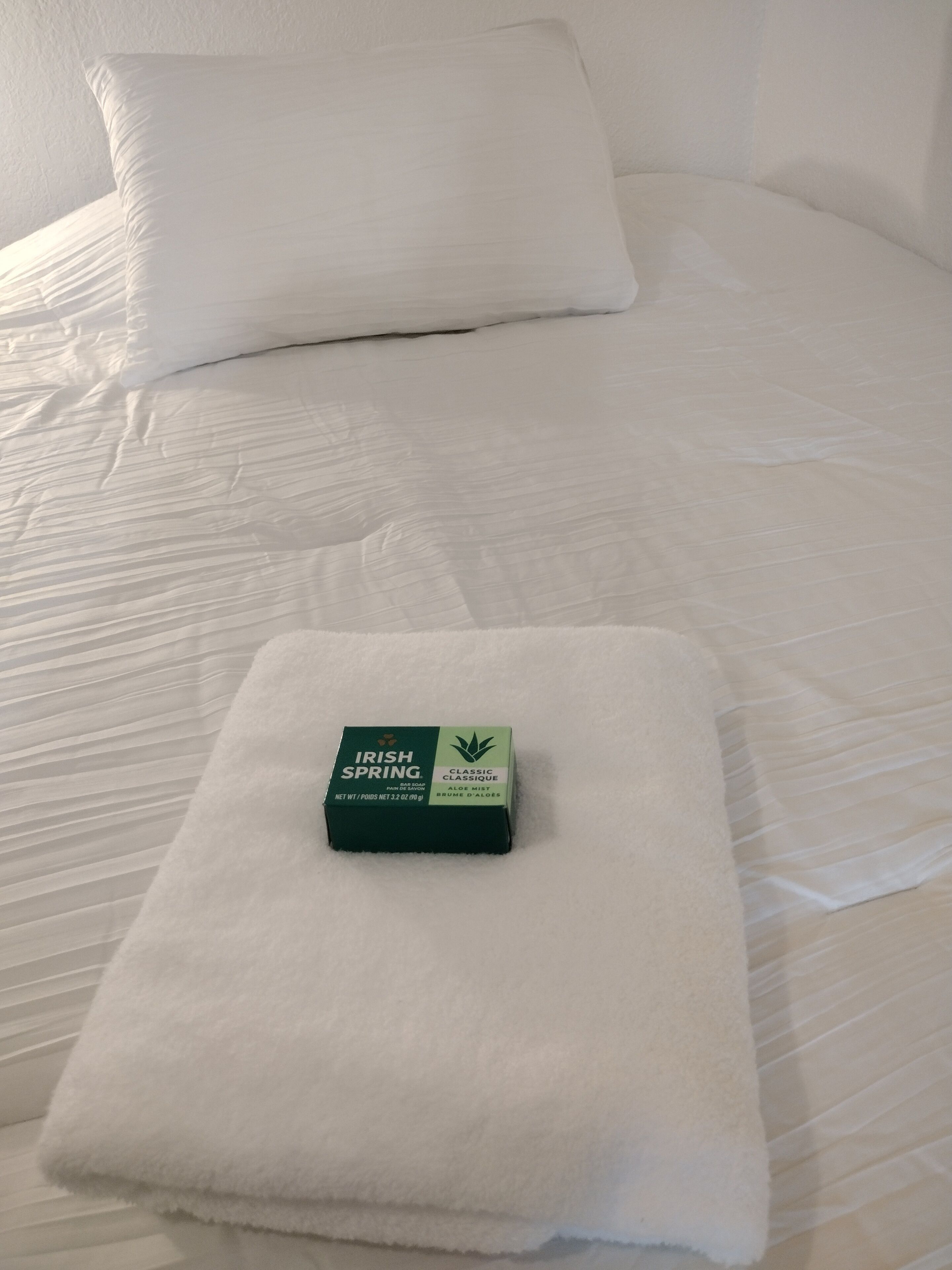 Un lit bien fait, avec un oreiller et une boîte de gel douche Irish Spring Classic Aloe Mint.