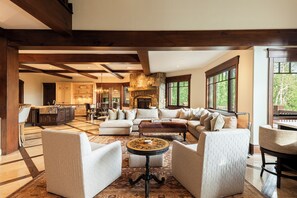 A spacious living area with a fireplace, large windows, and a kitchen in the background. - Ski-In/Ski-Out 6BR Luxury Estate with Indoor Pool, Hot Tub & Theater at The Colony, Sleeps 26 (Park City)