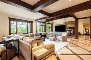 A spacious living room with a large sectional sofa, a flat-screen TV, and a stone fireplace. - Ski-In/Ski-Out 6BR Luxury Estate with Indoor Pool, Hot Tub & Theater at The Colony, Sleeps 26 (Park City)