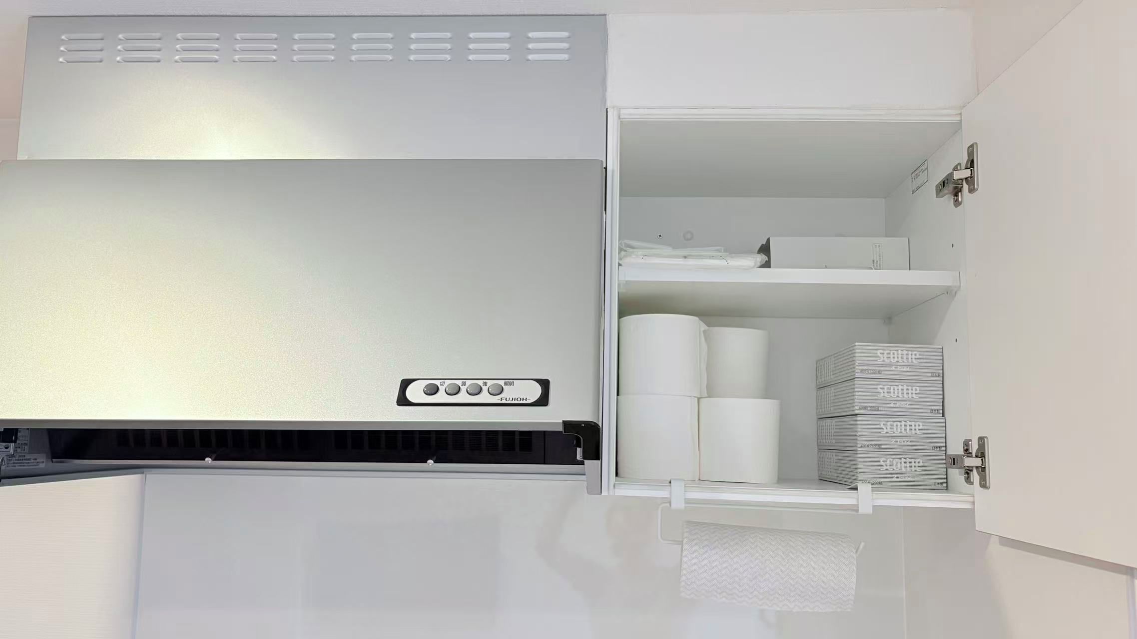 A white refrigerator with a control panel, a freezer compartment, and a shelf with paper towels and boxes.