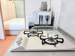 A kitchen with a white stove, a bed in the background, and a window with curtains. - SERENE · Sekime-Takadono · 403 | 2BR | Sleeps 3 | Direct Access to Umeda & Tennoji (大阪市)
