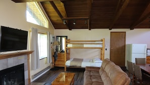 A room with a fireplace, a television, a bunk bed, a sofa, a dining table, and chairs. - 2 Queen Beds, 1 Bunk Bed, Kitchen, Fireplace (Packwood)