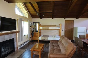 Een kamer met een open haard, een televisie, een stapelbed, een bank, een eettafel en stoelen.