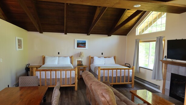 A room with two wooden beds, a sofa, a table, a fireplace, and a television. - 2 Queen Beds, 1 Bunk Bed, Kitchen, Fireplace (Packwood)