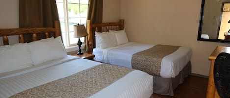 A hotel room with two beds, a wooden headboard, a mirror, and a window with curtains.