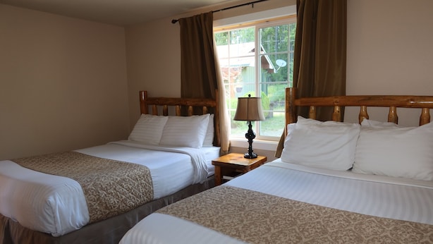 A room with two beds, a nightstand with a lamp, and a window with curtains. - 2 Queen Beds, 1 Sofa Bed, Kitchen. No Pets Allowed (Packwood)
