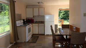 A compact kitchen with a stove, microwave, and refrigerator, a dining table with chairs, and a view of greenery outside. - 2 Queen Beds, 1 Sofa Bed, Kitchen. No Pets Allowed (Packwood)