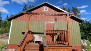 A wooden cabin with a green exterior, a door marked '15', a small porch with a chair, and a staircase leading to the entrance. - 2 Queen Beds, 1 Sofa Bed, Kitchen. No Pets Allowed (Packwood)