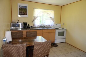 Een kleine keuken met een eettafel, stoelen, een magnetron, een fornuis en een spoelbak.