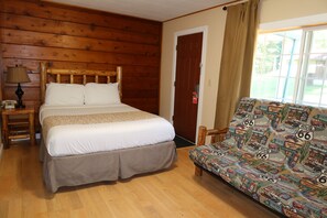 Een kamer met een bed met houten hoofdbord, een bank met een wegenkaart dessin, een lamp en een deur.