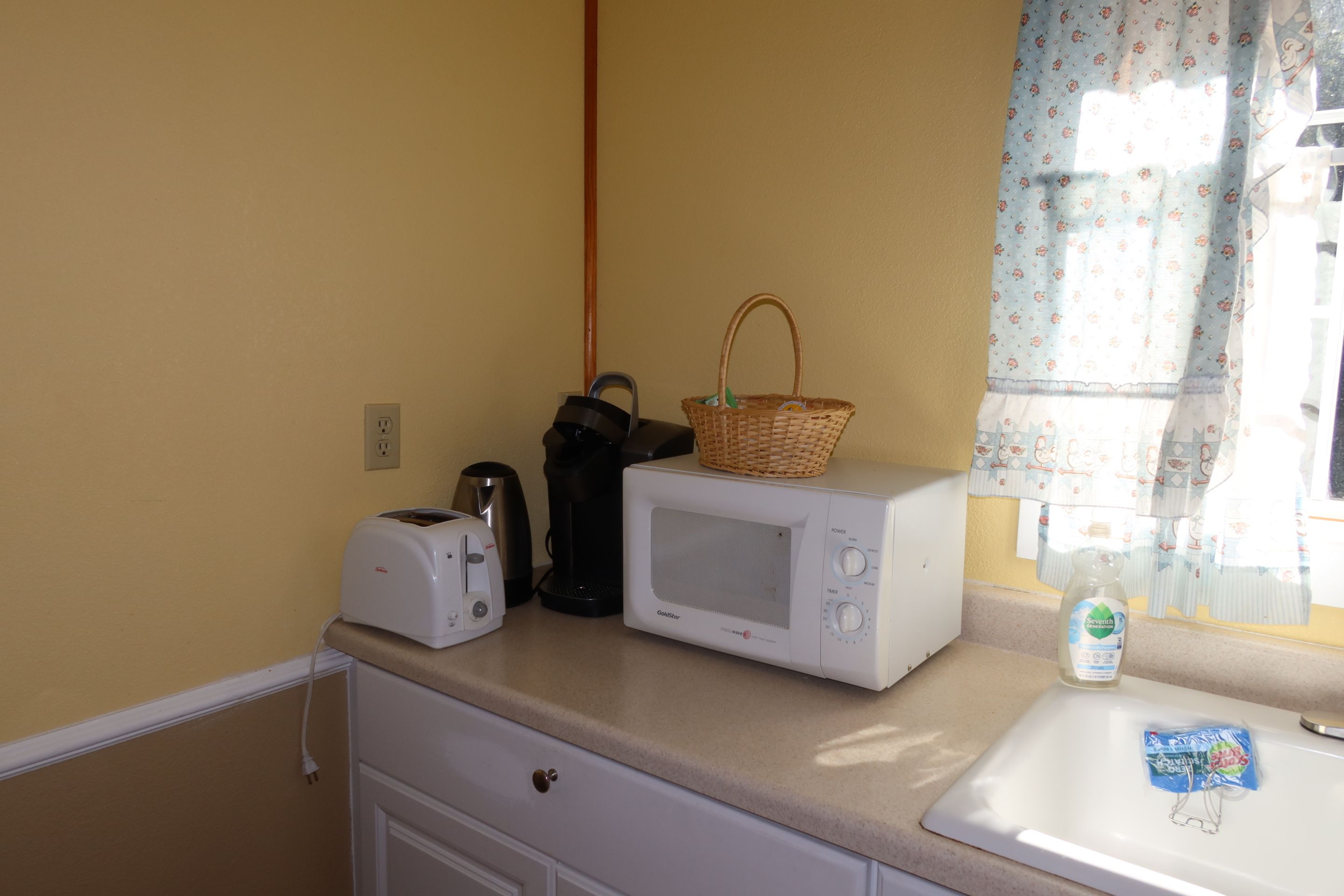 A kitchenette with a toaster, a microwave, and a basket on the counter.