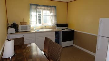 A compact kitchen with a sink, stove, microwave, and a dining table with chairs.