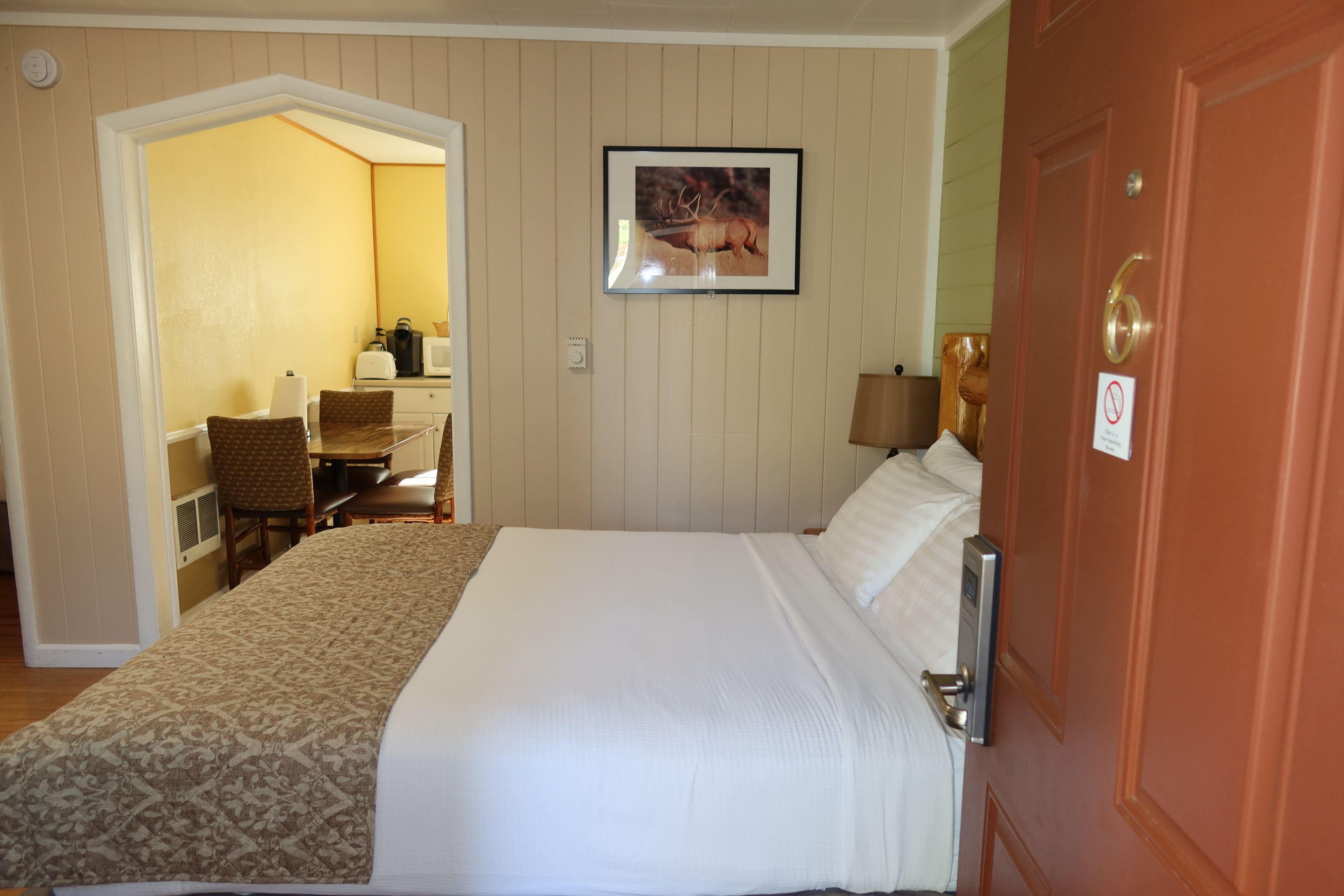 A hotel room with a bed, a desk with a chair, a lamp, and a picture on the wall.