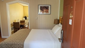 A hotel room with a bed, a desk with a chair, a lamp, and a picture on the wall.