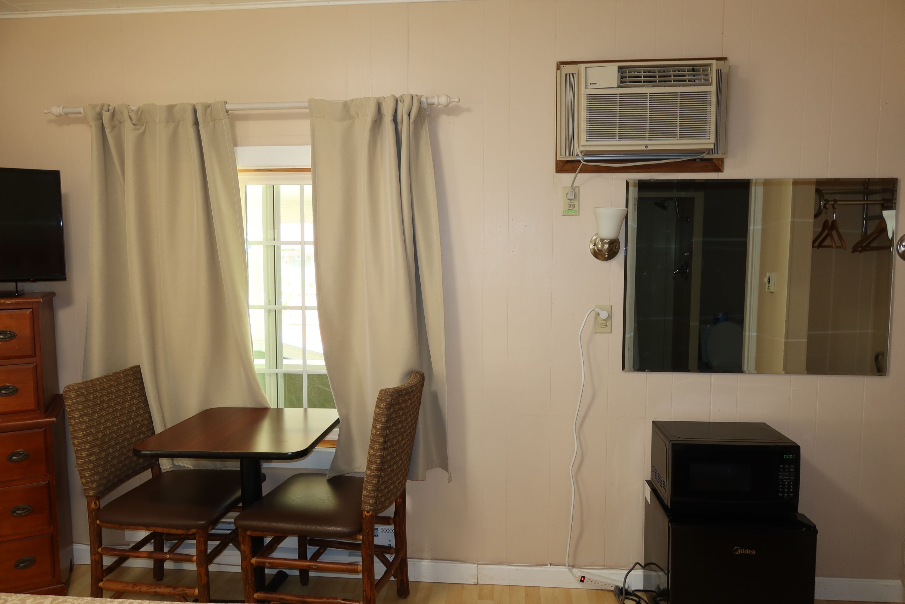 A room with a table and chairs, an air conditioner, a mirror, and a microwave.