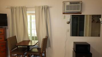 A room with a table and chairs, an air conditioner, a mirror, and a microwave.