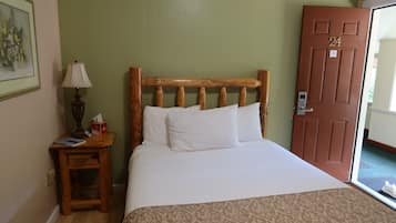 A room with a wooden headboard bed, a bedside table with a lamp, and a door with a number.