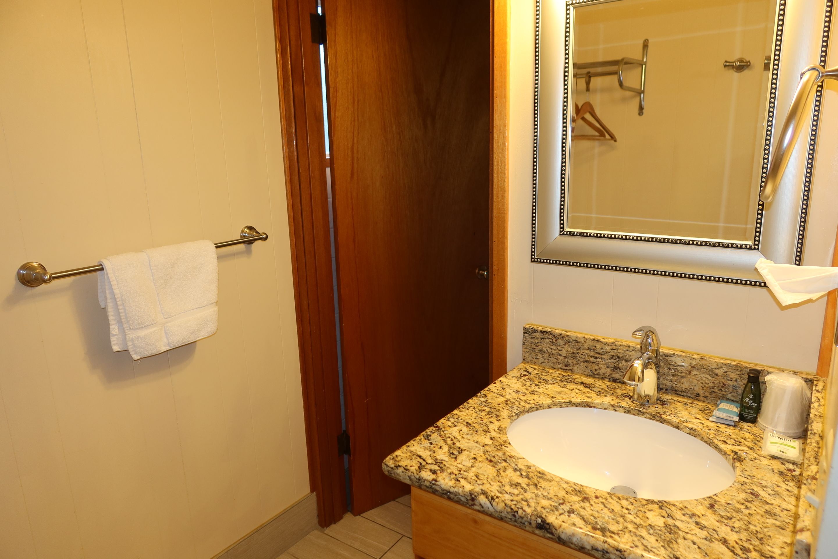 Une salle de bain avec un lavabo doté d’un plan de travail en granit, un miroir avec un cadre décoratif et un porte-serviettes sur lequel est posée une serviette blanche.