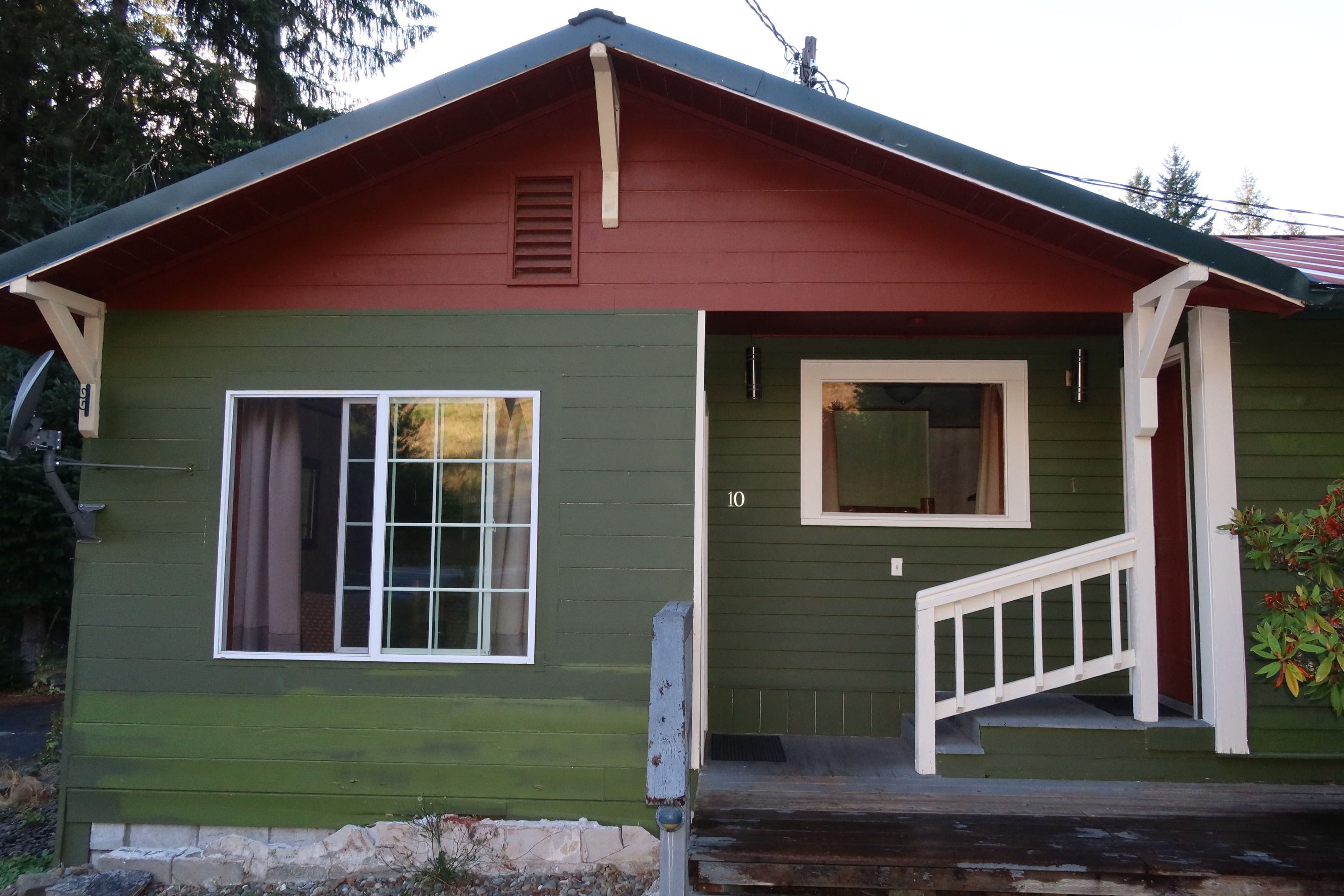 A green house with a red roof, a white front door, and a small porch.