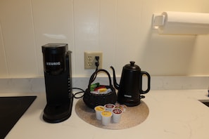 Una kitchenette equipada con una cafetera Keurig, un hervidor y un cesto de cápsulas de café.