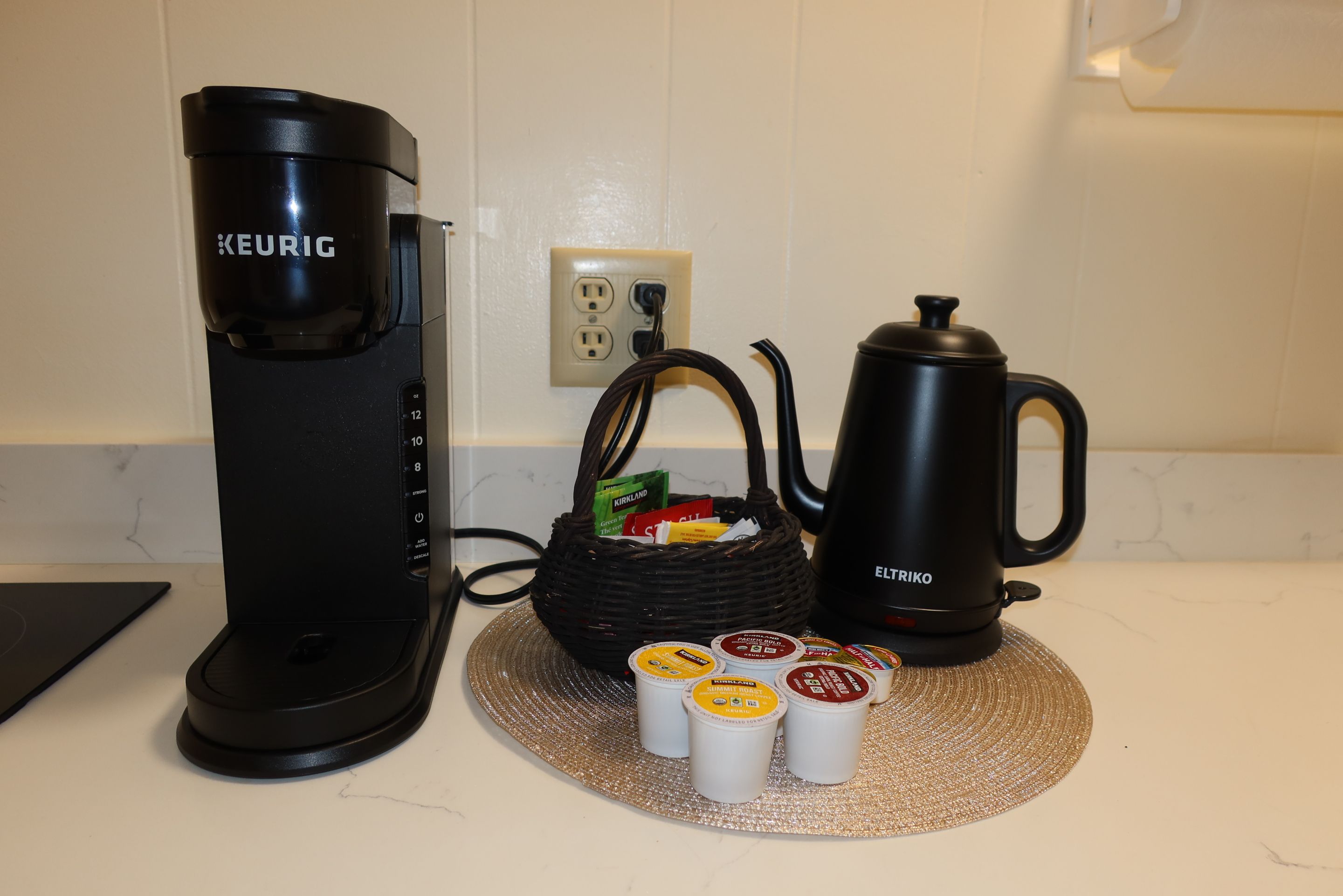 Une machine à café, une bouilloire et des dosettes de café sur un plan de travail de cuisine.