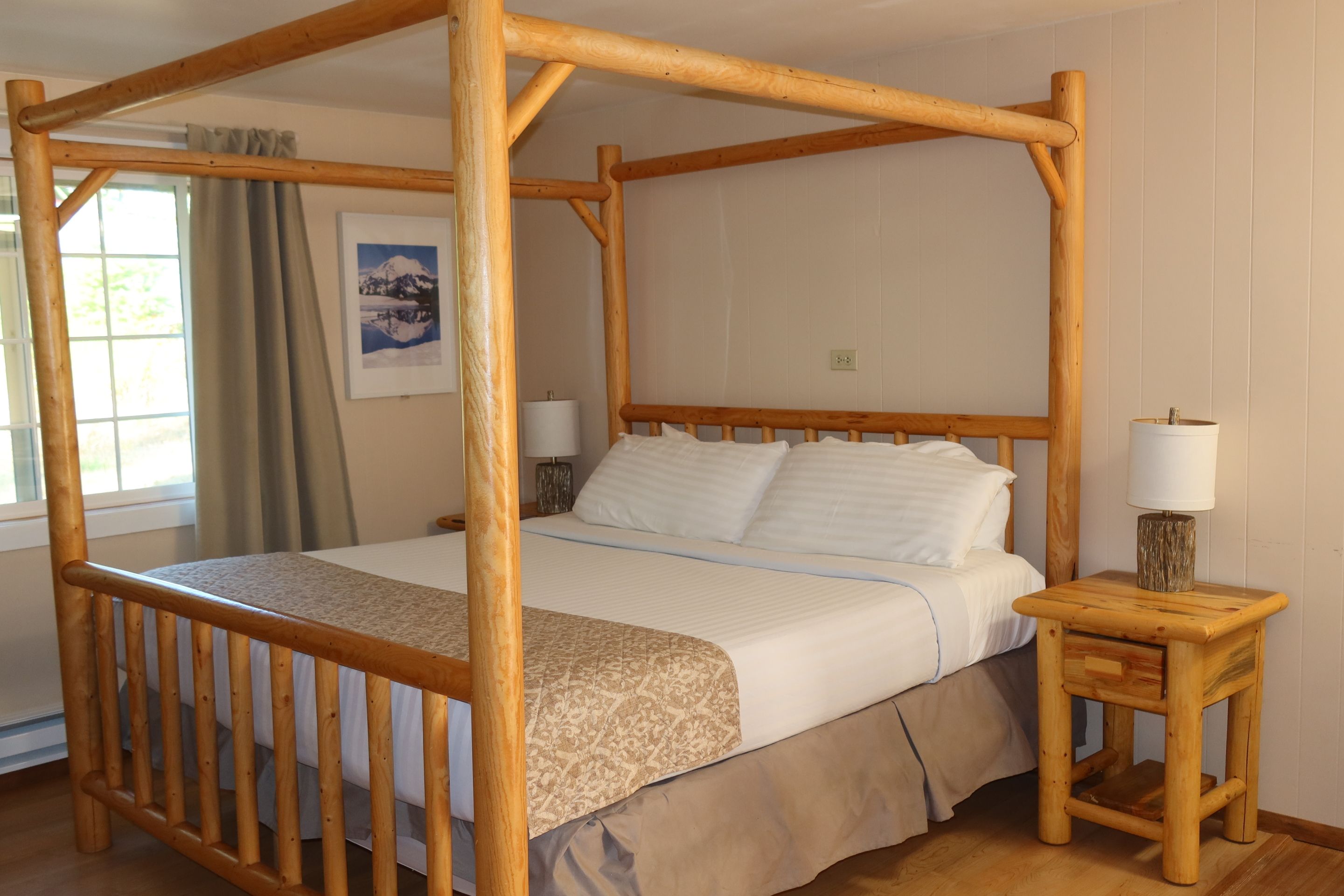 A four-poster bed with a wooden frame, a bedside table with a lamp, and a window with curtains.