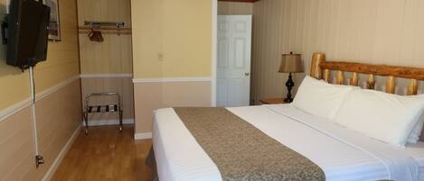 Quarto de hotel com cama, uma cadeira, televisão, cabideiro e porta.