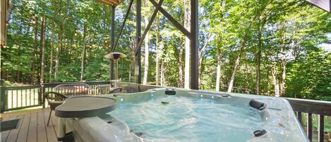 A hot tub on a wooden deck with a view of a forest.